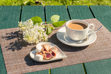 On the garden table is a cup of coffee with cream, sweet biscuits on a plate.