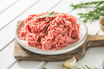 Fresh Raw Beef Minced Meat with herbs and rosemary on wooden board on a light background, banner, menu, recipe place for text, top view,