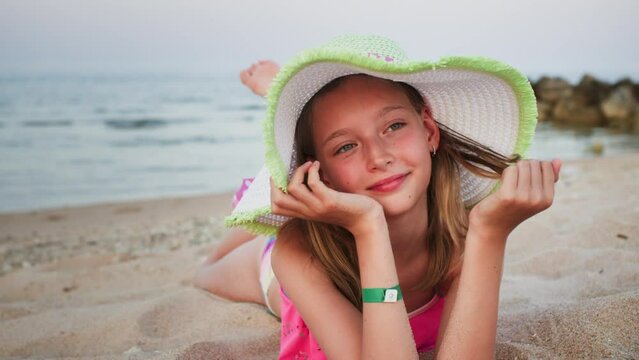 Portrait Of Teen Girl In Hat Is Dreaming Lying On The Sea Beach. Traveling, Tourism, Resting On Vacations Concept. Beautiful Seascape With Sand And Rocks. Cute Sweet Teen Girl Is Relaxing Chilling.