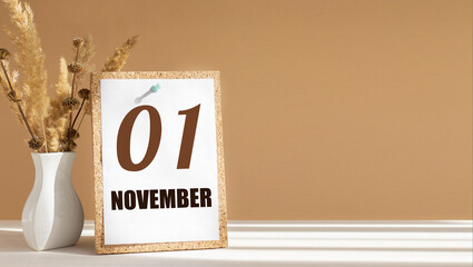 november 1. 1th day of month, calendar date.White vase with dead wood next to cork board with numbers. White-beige background with striped shadow. Concept of day of year, time planner, autumn month