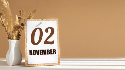 november 2. 2th day of month, calendar date.White vase with dead wood next to cork board with numbers. White-beige background with striped shadow. Concept of day of year, time planner, autumn month