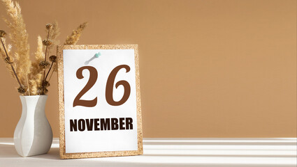 november 26. 26th day of month, calendar date.White vase with dead wood next to cork board with numbers. White-beige background with striped shadow. Concept of day of year, time planner, autumn month