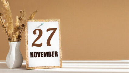 november 27. 27th day of month, calendar date.White vase with dead wood next to cork board with numbers. White-beige background with striped shadow. Concept of day of year, time planner, autumn month