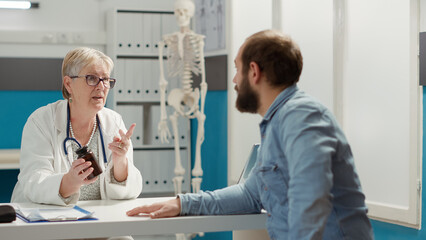 Obraz premium Female physician explaining prescription medicine in bottle, giving pills, drugs and medication to young patient at checkup visit. Disease treatment with vitamins and painkillers in flask.