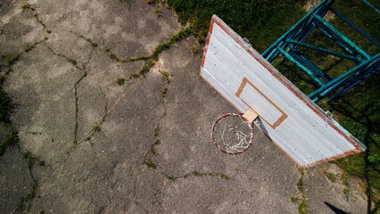Old basketball backboard. Made from boards. Peeling paint and a battered basket. There is an old cracked asphalt on the site. Shot from above. Aerial photography.