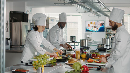 Team of cooks slicing vegetables on cutting board for meal preparation in restaurant kitchen. Man and woman cooking gourmet food dish with organic ingredients, working on culinary recipe.