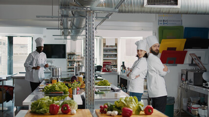 Portrait of professional chefs posing with arms crossed on camera, working in restaurant kitchen to...