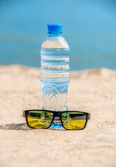 A bottle of drinking water and sunglasses on the sea beach
