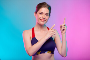 Smiling sporty woman in fitness sportswear pointing finger to empty space. Female fitness portrait isolated on neon multicolor background.