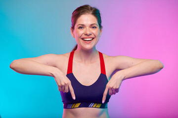 Fototapeta na wymiar Smiling sporty woman in fitness sportswear pointing finger down. Female fitness portrait isolated on neon color background.