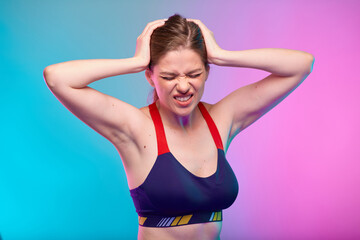 Fototapeta na wymiar Woman with headache pain touching her head with eyes closed. Girl in sportswear. Female fitness portrait isolated on neon pink blue color background.