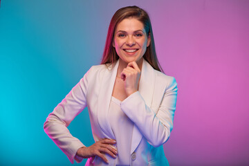 Smilng business woman touching her chin, face, isolated portrait with neon lights colors effect. Female model on neon colored background wearing white suit.