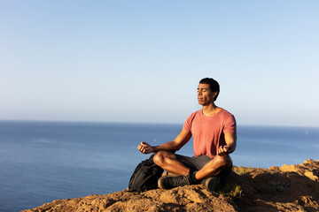 Naklejka na ściany i meble Young man meditating on top ocean cliff..