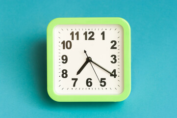 Minimal flat lay concept. Green analog clock on blue background.