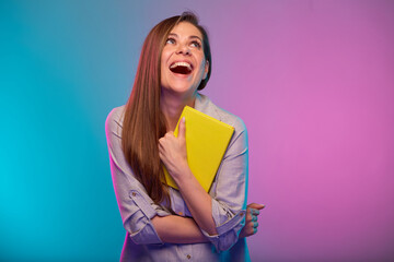 Happy teacher or student woman with open mouth looking up holding book, portrait with neon lights colors effect. Female model isolated on neon background