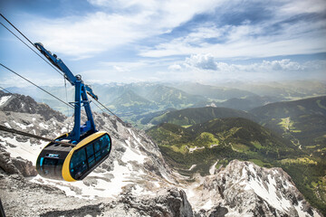 Mountain panorama - Cable car drives on mountain. Snow on mountain. Summer in the valley....