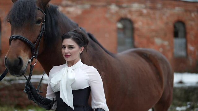 a woman in a black corset and long gloves leaned against the neck of a bay horse near a brick building