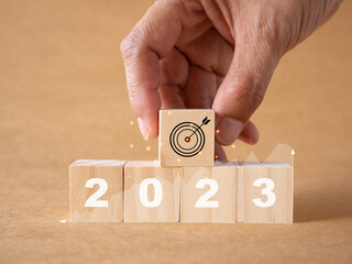 Business growth target. Businessman hand holding wooden cubes with number 2023, graph and target icon on brown paper.background. Business development strategy, advancement and goal concept..