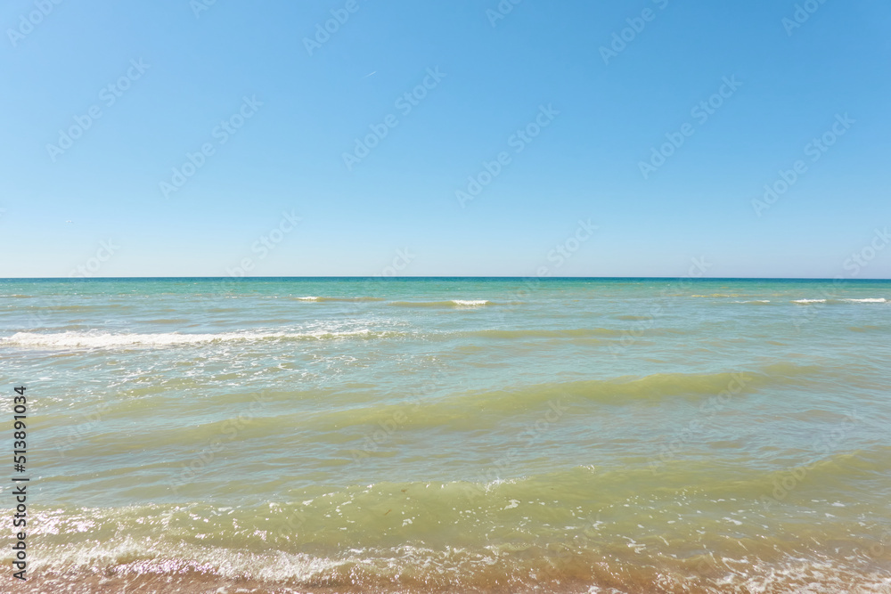 Wall mural Baltic sea shore on a sunny day. View from a sandy beach sand dunes). Clear blue sky, turquoise water. Idyllic seascape, landscape. Pure nature, ecology, eco tourism, vacations. Spring, early summer