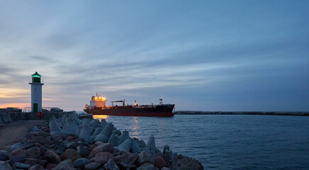 Large oil chemical tanker ship arriving to the cargo port terminal at sunset. Breakwaters, promenade to the lighthouse. Baltic sea, Ventspils, Latvia. Transportation, logistics theme. Panoramic view - 513892068