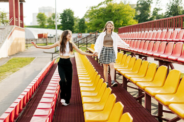 Fototapeta na wymiar Two teenage girls walk together through the stands of the school stadium, talking, holding hands, best friends return home after training