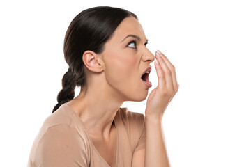 Profile of a young frowning woman checks her breath with her palm on a white background