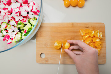 Fototapeta na wymiar Close-up of female hands cutting fresh yellow cherry tomatoes on cutting board at home kitchen