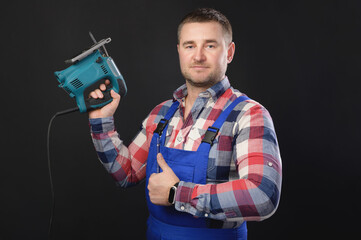 Portrait of a caucasian male repairman in a work uniform with an electric jigsaw in your hand Showing thumbs up. Studio portrait of an artisan businessman