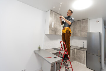 electrician, a male electrician is standing on the stairs holding wiring in his hands and stripping, repairing light at home, repair work, call master, electrician man repairing light