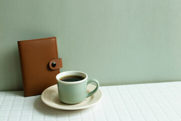 Cup of coffee and diary notebook on white desk. khaki green wall background