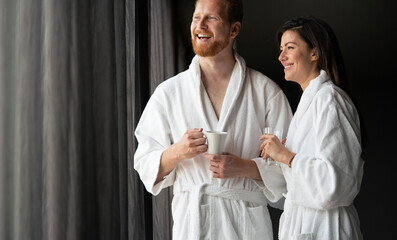 Happy young couple in white bathrobes drinking coffee together. Hotel, travel, relationships concept