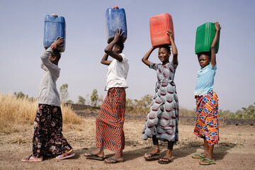 Busy teenagers lined up with heavy water canisters on their heads, symbolizing the role and...