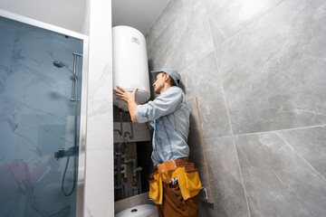 Plumber installing electric heating boiler. Young handyman in uniform setting up electric heating boiler at home