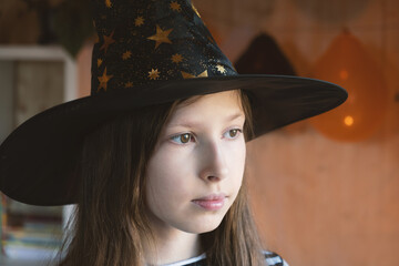 Halloween. Sad pensive girl in witch costume celebrating Halloween. Copy space. Portrait of unhappy little girl wearing Halloween hat masquerade as a witch