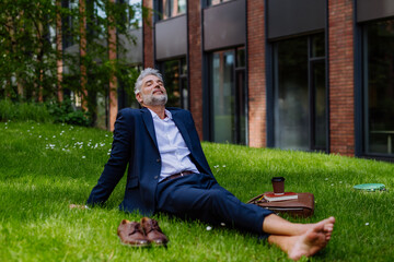 Mature businessman resting and sitting barefoot in park, feeling free, escaping from work, work...
