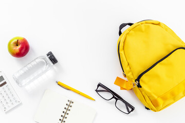 Back to school concept. Yellow school backpack with supplies water and apple - obrazy, fototapety, plakaty