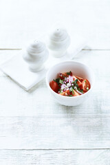 Simple salad with cherry tomatoes, red onion and fresh herbs. Bright wooden background. Copy space.