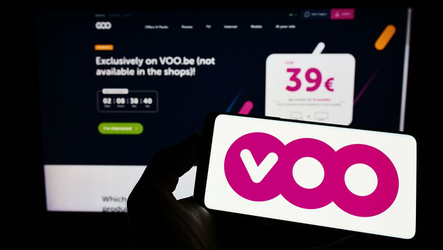 Stuttgart, Germany - 06-25-2022: Person holding mobile phone with logo of Belgian telecommunications company Voo SA on screen in front of business web page. Focus on phone display.