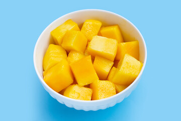 Yellow mango cube slices in white bowl on blue background.