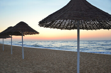 Landscape with rattan umbrellas on the seashore  without people  in the morning before sunrise . Summer vacation near the sea, travelling  concept.