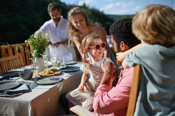 Family with kids having fun at barbecue party dinner on patio, people sitting at table on patio and talking