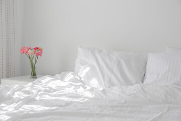 Close up shot of an empty unmade bed with white bedsheets and the nightstand with bouquet of...