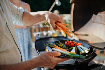 Unrecognizable man preparing vegetables for grilling during family summer garden party, close-up