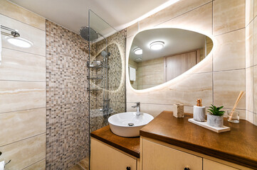 Modern bathroom with silver rain head, hand held shower, sink, mirror on the wall with backlight,...