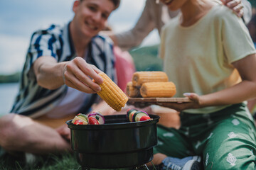Close-up of young friends putting corn on grill and having barbecue when camping in campground.