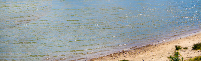 Banner with a copy of the space on the left, Sandy riverbank with grass, coastline with blue water, top view