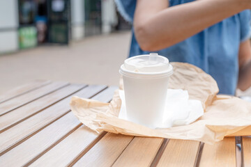 closeup of woman eating fast food in street cafe, mockup white coffee cup