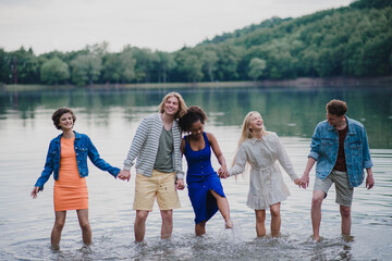 Multiracial group of young friends holding hands and standing in lake in summer.