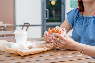 closeup of woman hands holding hamburger, woman eating fast food at street cafe