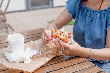 closeup of woman hands holding hamburger, woman eating fast food at street cafe